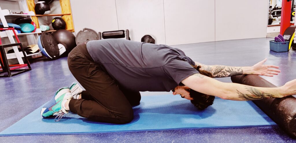 A woman is stretching on the floor with another person.