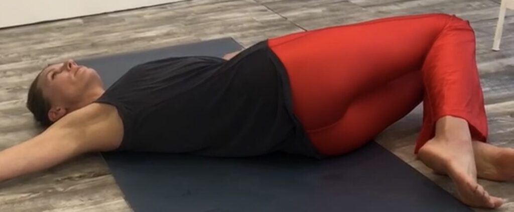A woman is stretching on the floor with another person.